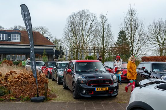 Een rij auto’s op een parkeerplaats met een vrouw in een gele jas op de achtergrond.