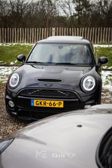 Zwarte Mini Cooper met Nederlandse kentekenplaat, geparkeerd op een sneeuwachtige ondergrond.